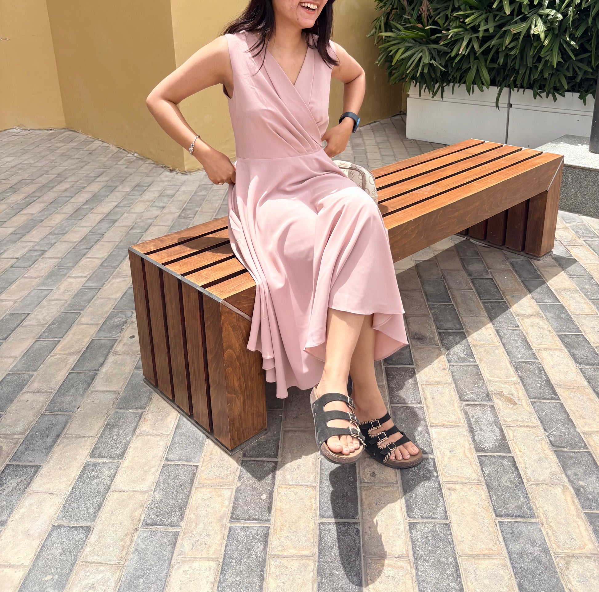 Woman in a pink dress sitting on a wooden bench outdoors.