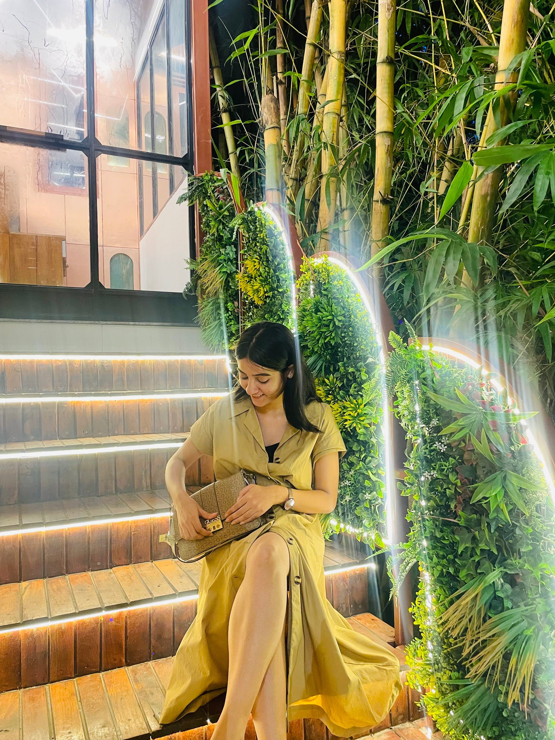 Woman in a yellow dress sitting on steps with greenery around