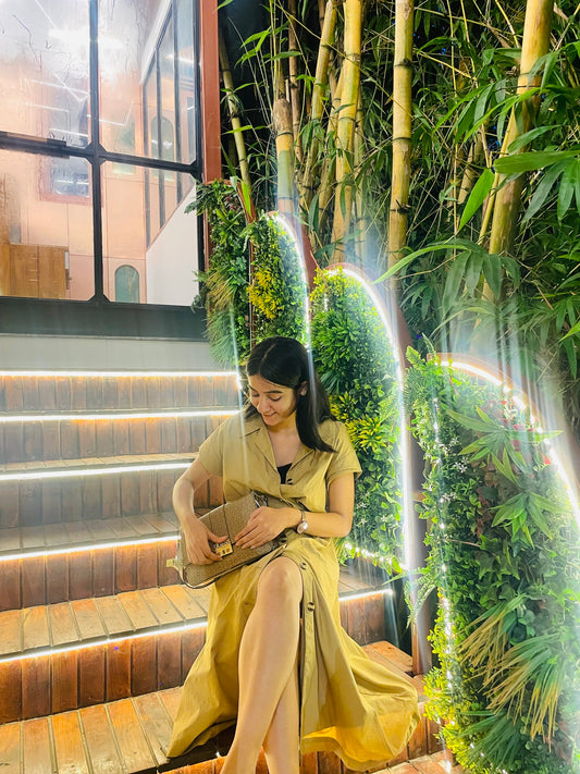 Woman in a yellow dress sitting on steps with greenery around