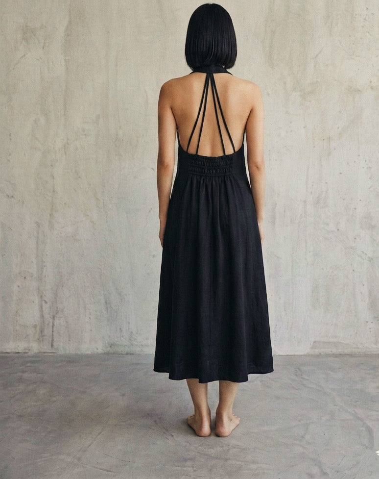 Back view of women’s black halter midi dress featuring open back strap detailing and smocked waist