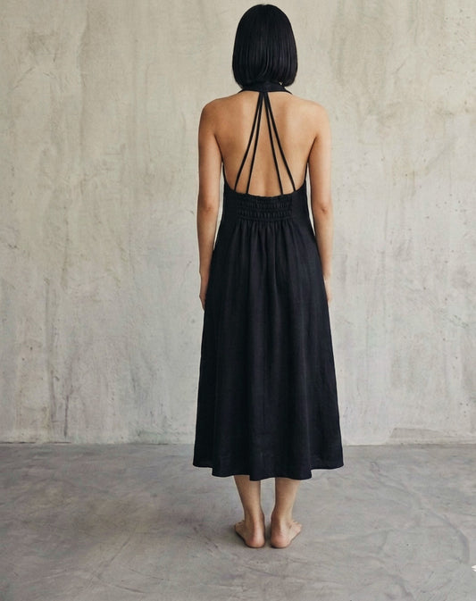 Back view of women’s black halter midi dress featuring open back strap detailing and smocked waist